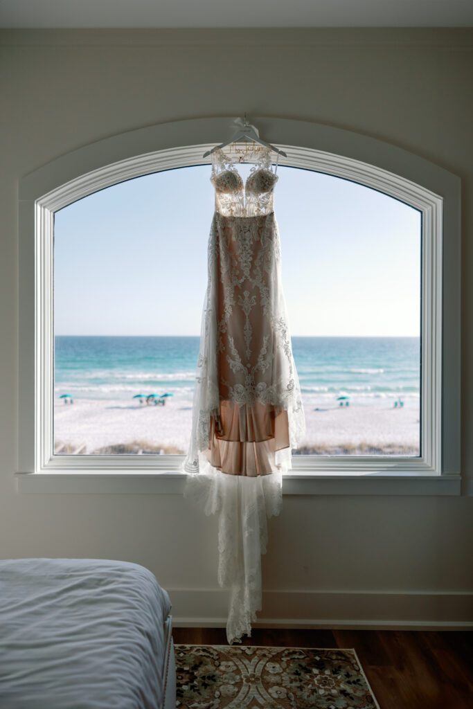 Bridal gown hanging in large window of a luxury bedroom for a beach elopement wedding in Destin, FL